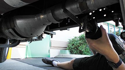 A mechanic inspecting the underside of a vehicle in a garage.